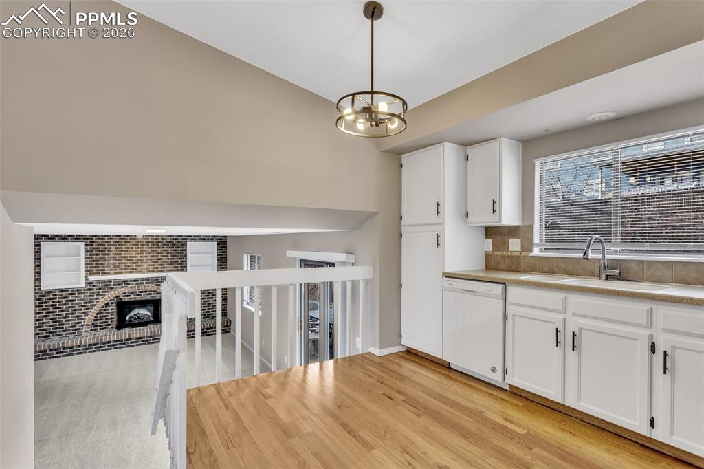 Image 9 of 30: Kitchen with a fireplace, white cabinetry, white dishwasher, light wood-sty