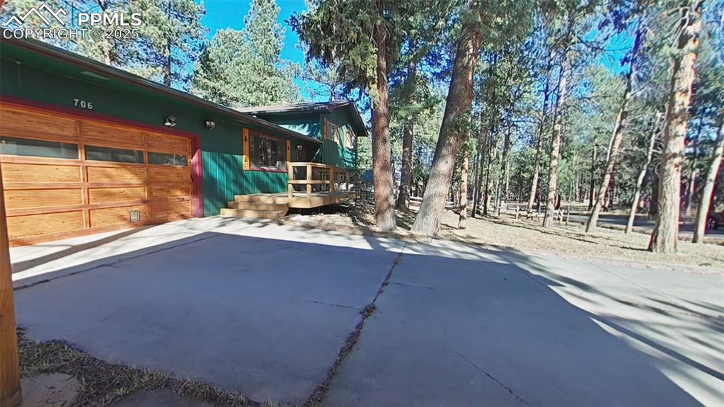 Image 12 of 25: View of home front featuring driveway, an attached garage, and a wooden dec