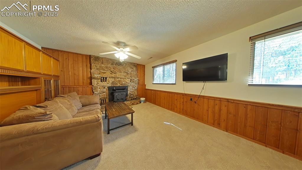 Image 19 of 25: Carpeted family room featuring wood walls, wainscoting, a wood stove, a tex