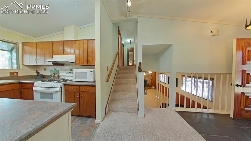 Image 5 of 25: Kitchen with white appliances, lofted ceiling, brown cabinets, under cabine