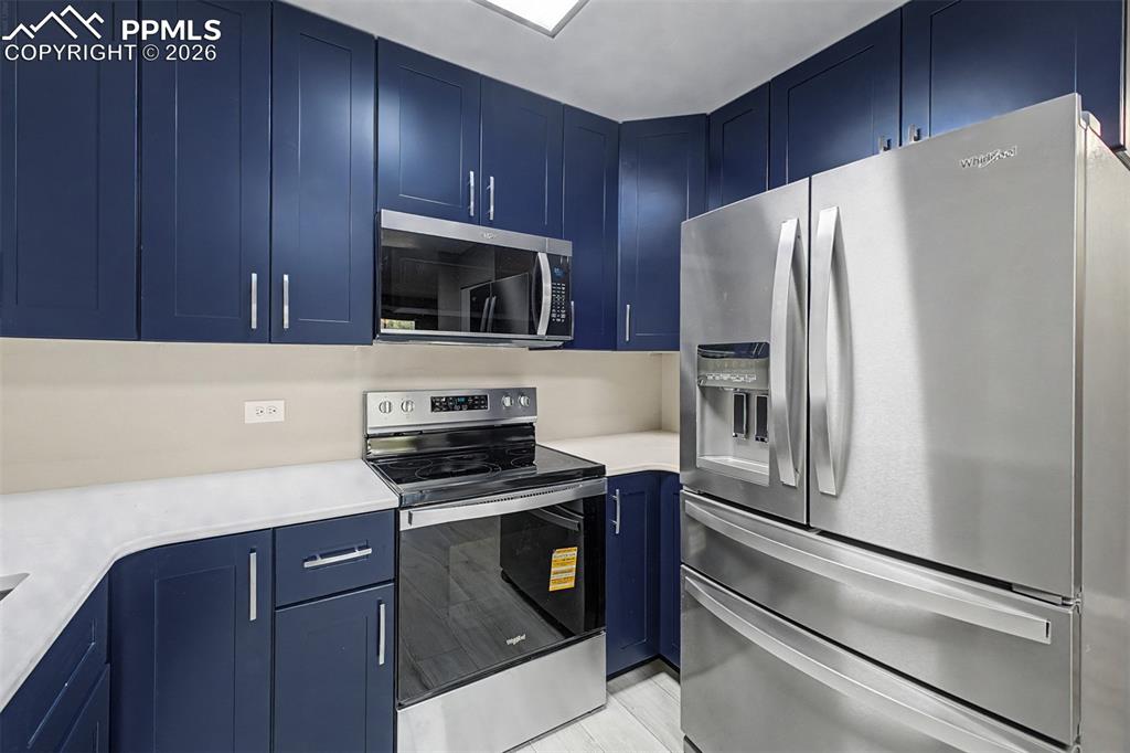 Image 2 of 42: Contemporary kitchen featuring navy blue cabinetry, stainless steel applian