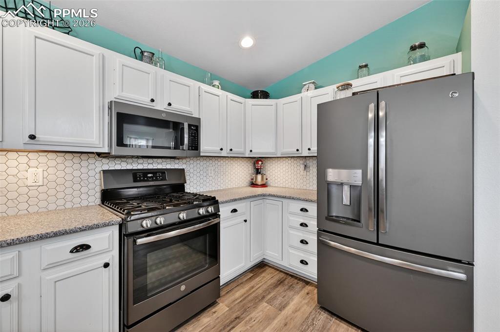 Image 20 of 47: Kitchen with stainless steel appliances, white cabinets, light stone counte