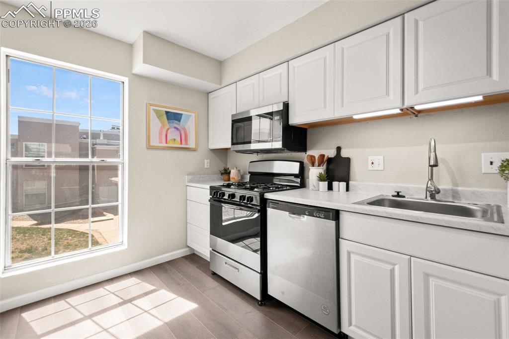 Image 13 of 27: The kitchen features white cabinetry, stainless steel appliances, and a win