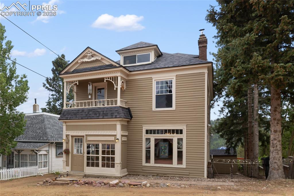 Caption: View of front facade with a chimney, a balcony, entry steps, and roof with shingles