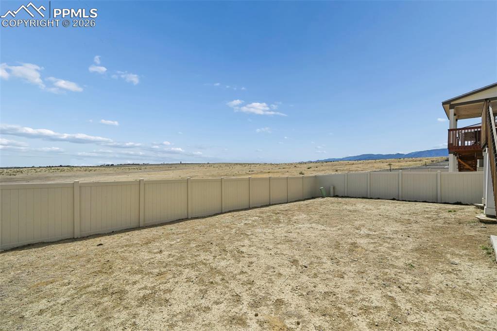 Image 37 of 43: Expansive rear yard with a perimeter fence, a partially covered deck, and d