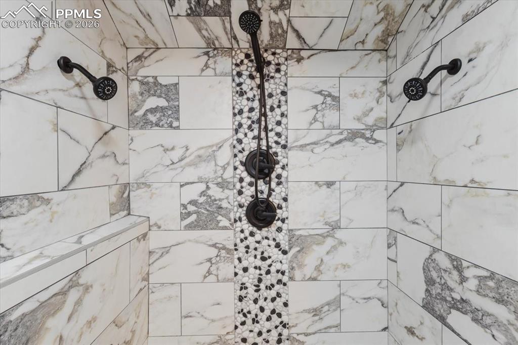Image 26 of 45: Shower enclosure featuring large format marble-look tile, a mosaic river ro