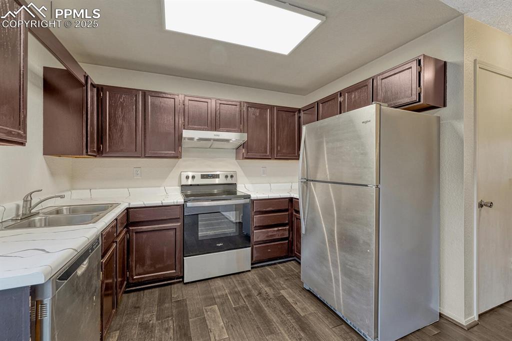 Image 15 of 32: Kitchen with stainless steel appliances, light countertops, dark wood-style