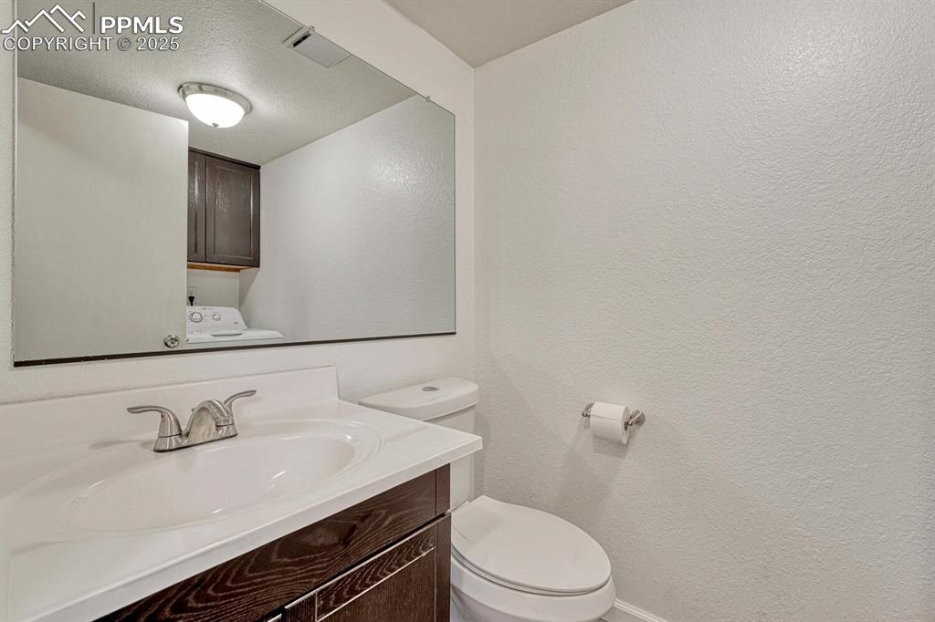 Image 18 of 32: Half bath featuring vanity, a textured ceiling, a textured wall, and washer