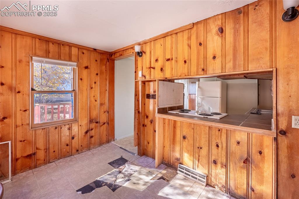Image 10 of 30: Kitchen with white appliances, wood walls, tile countertops, and brown cabi
