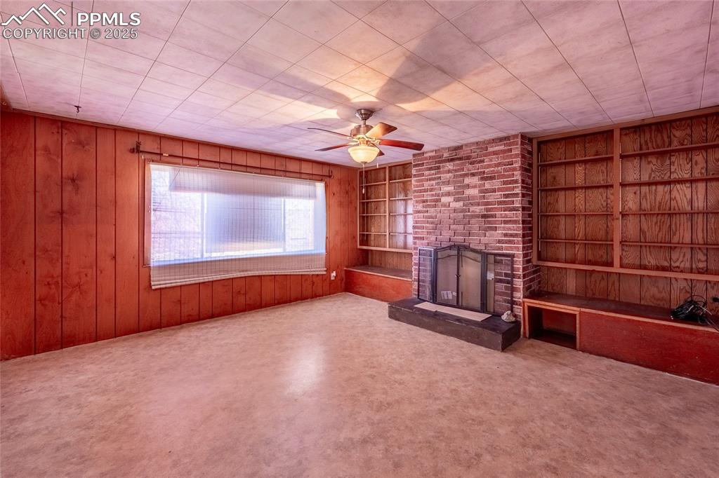 Image 4 of 30: Unfurnished living room featuring built in features, a fireplace, wood wall