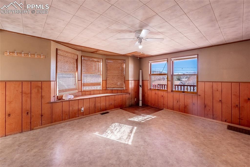 Image 6 of 30: Carpeted empty room with a ceiling fan, wooden walls, and wainscoting