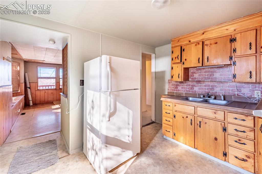 Image 9 of 30: Kitchen with freestanding refrigerator, tasteful backsplash, wood walls, wa