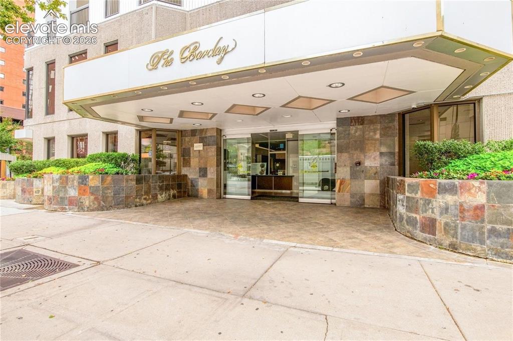 Image 32 of 35: Building entrance featuring a multi-toned stone facade, a prominent awning 