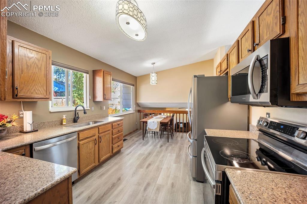 Image 2 of 47: Kitchen with stainless steel appliances, brown cabinetry, vaulted ceiling, 