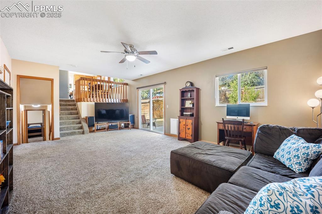 Image 24 of 47: Living room with stairs, carpet floors, and a ceiling fan