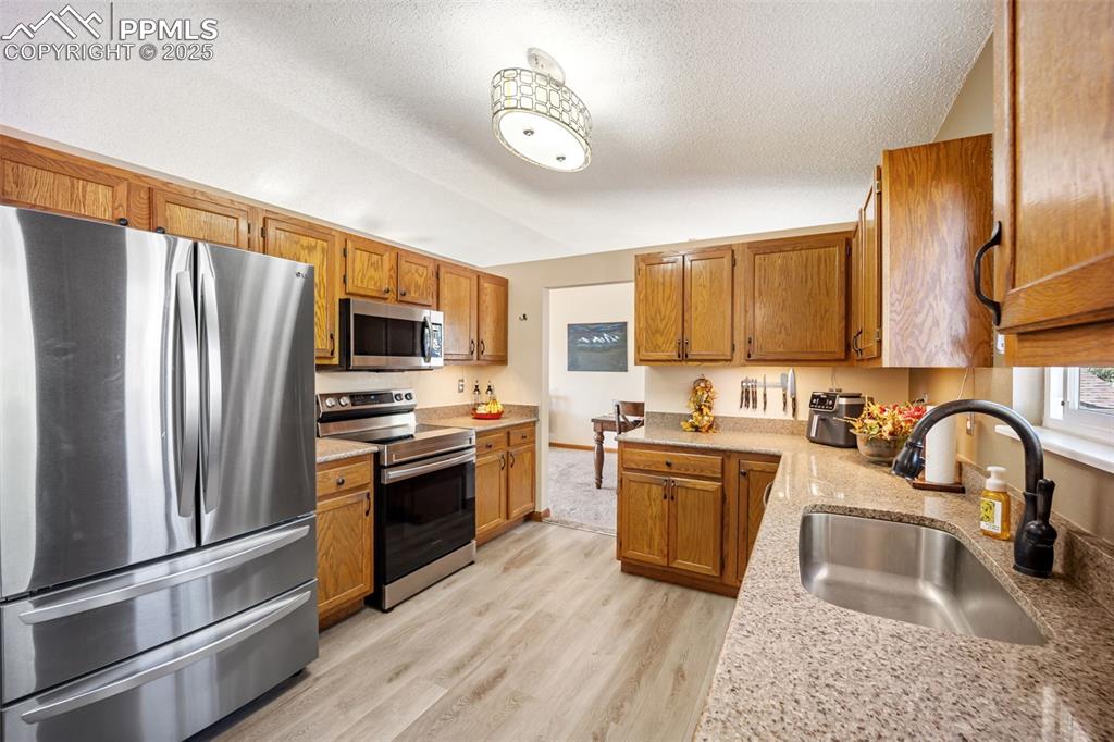 Image 8 of 47: Kitchen featuring stainless steel appliances, brown cabinetry, light wood-t