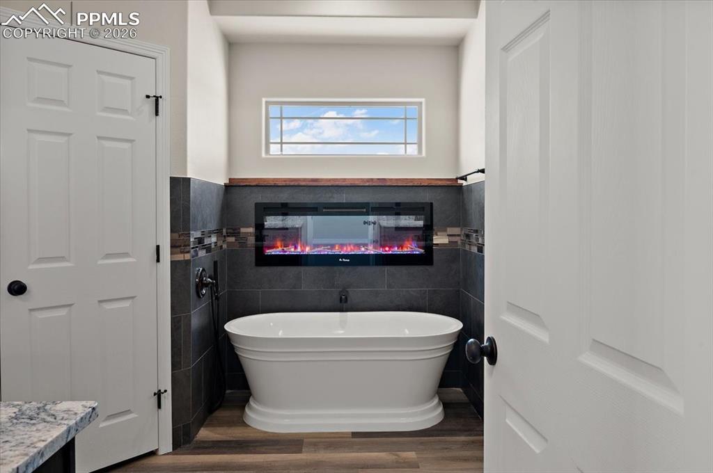 Image 18 of 40: Bathroom featuring tile walls, a freestanding bath, dark wood finished floo