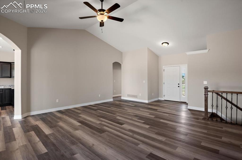 Image 2 of 40: Unfurnished living room with arched walkways, dark wood-style flooring, cei