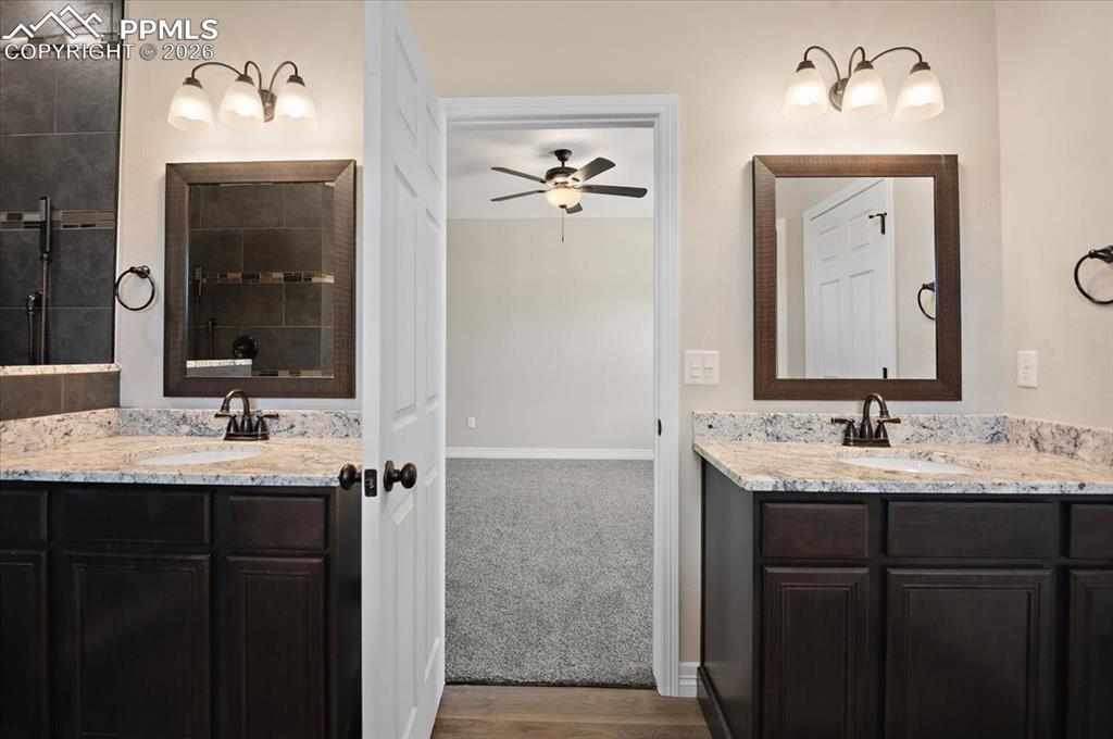 Image 23 of 40: Full bathroom featuring two vanities, a tile shower, a ceiling fan, and dar