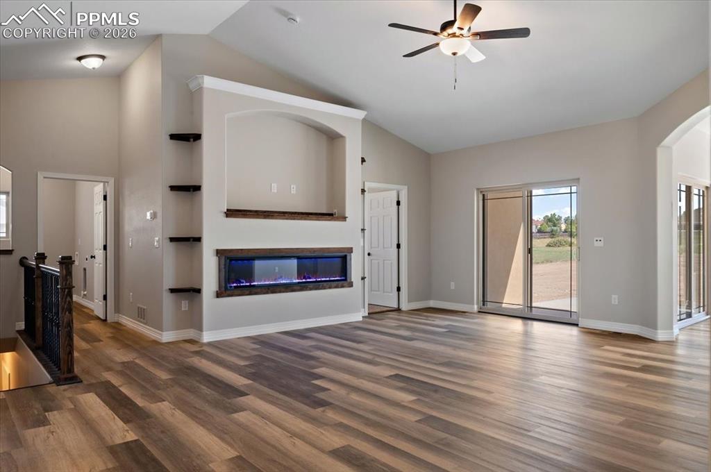 Image 4 of 40: Unfurnished living room featuring arched walkways, wood finished floors, ce