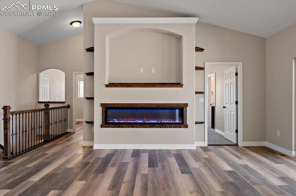 Image 6 of 40: Unfurnished living room with wood finished floors, lofted ceiling, and a gl