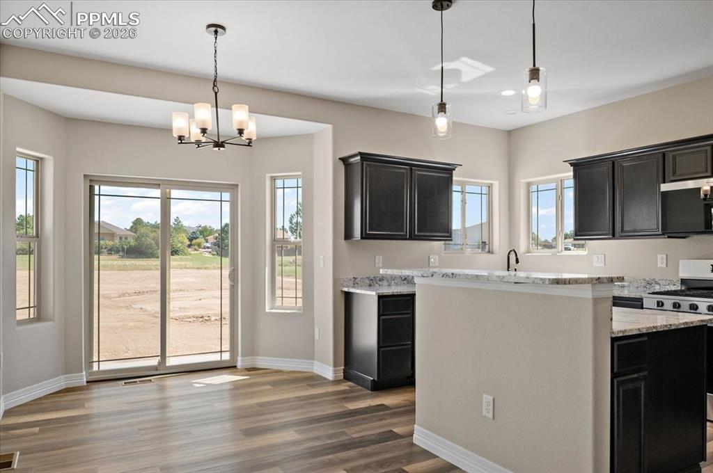 Image 7 of 40: Kitchen with dark cabinetry, a kitchen island, light stone counters, and de