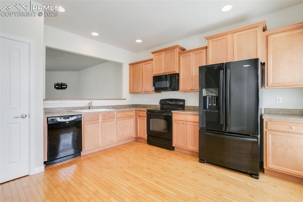 Image 12 of 28: Kitchen featuring light brown cabinets, black appliances, light wood-type f