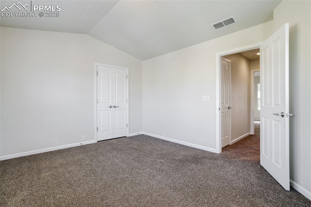 Image 16 of 28: Empty room featuring dark colored carpet and lofted ceiling
