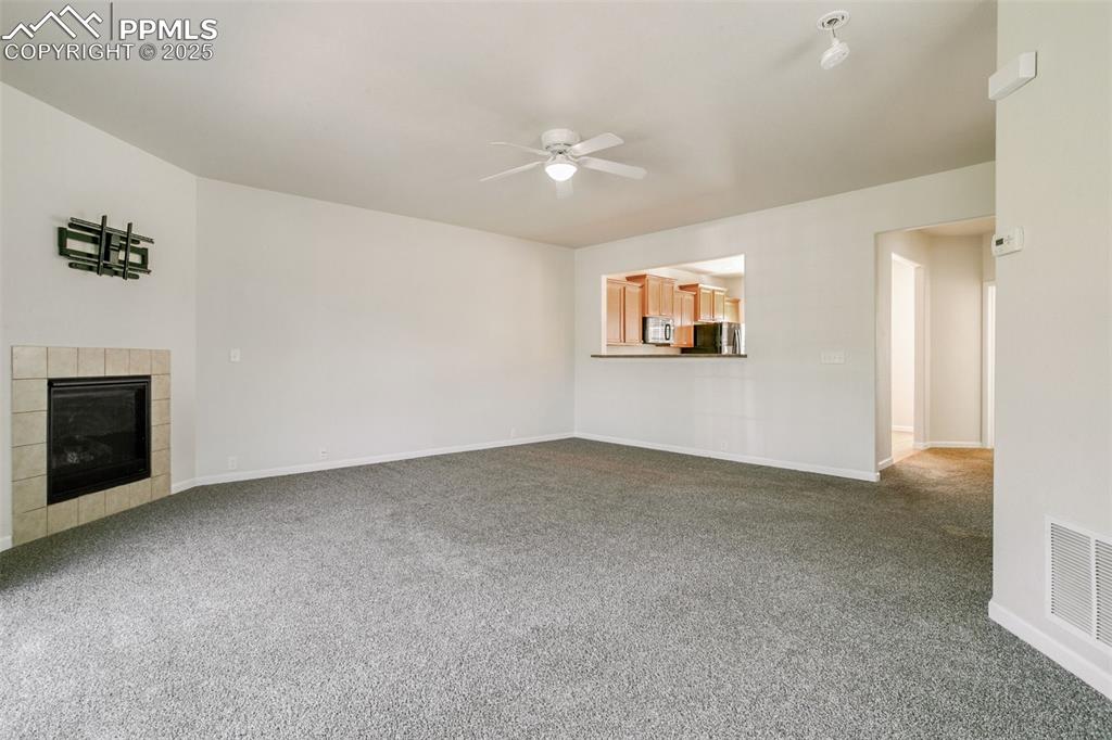 Image 5 of 28: Unfurnished living room with ceiling fan, dark carpet, and a tiled fireplac