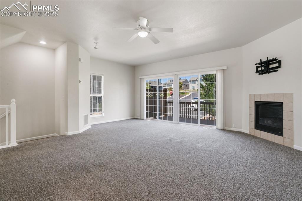 Image 7 of 28: Unfurnished living room with a tile fireplace, carpet floors, a ceiling fan
