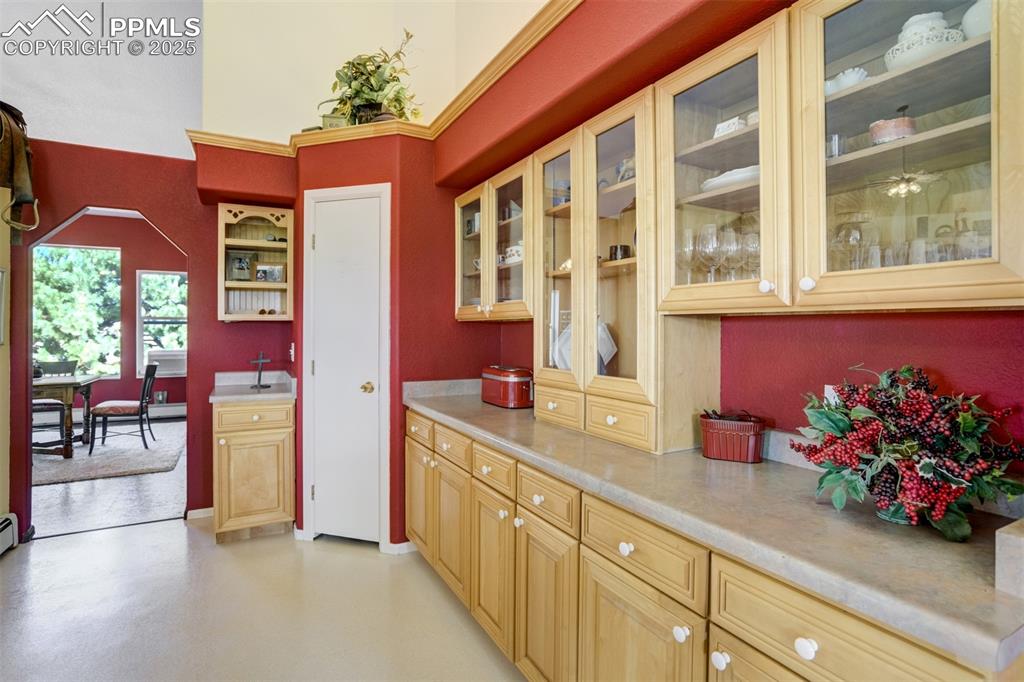 Image 11 of 50: Kitchen featuring light countertops, glass insert cabinets, and arched walk
