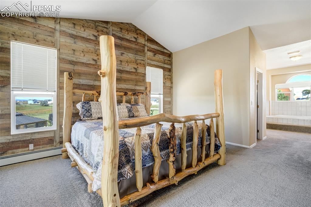 Image 13 of 50: Carpeted bedroom with lofted ceiling, wood walls, a baseboard radiator, and