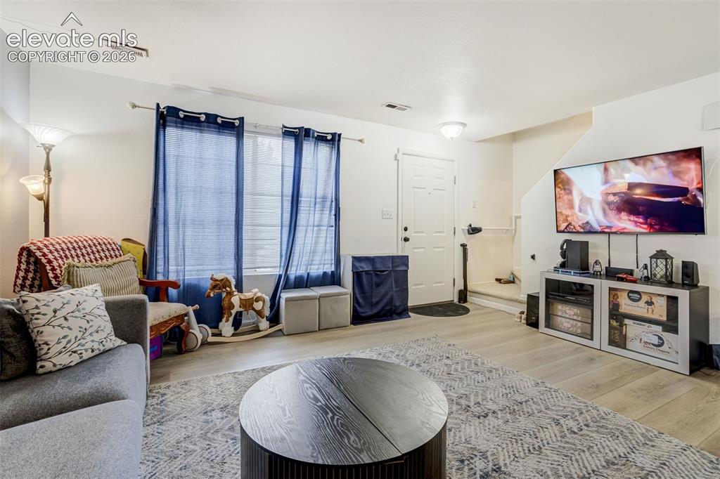 Image 14 of 43: Spacious living area featuring light wood-finish flooring, white walls, and