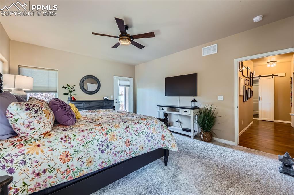 Image 15 of 47: Carpeted bedroom with a barn door and ceiling fan