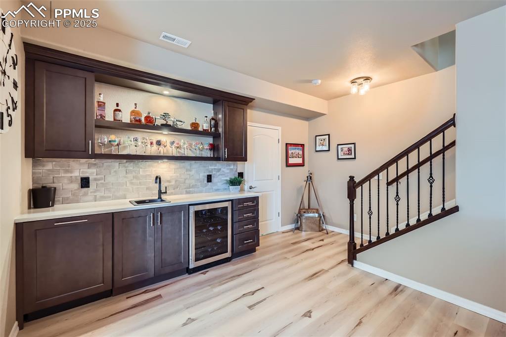 Image 28 of 47: Indoor wet bar with wine cooler, backsplash, light wood-style flooring, and