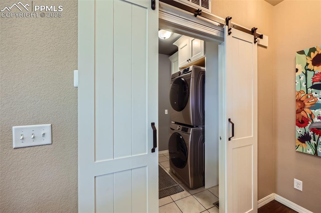 Image 29 of 47: Laundry room with stacked washer / drying machine, cabinet space, a barn do