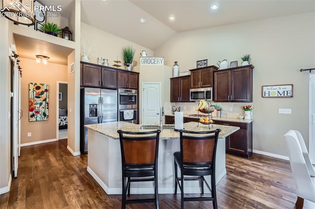 Image 8 of 47: Kitchen with high vaulted ceiling, dark brown cabinetry, a kitchen island w