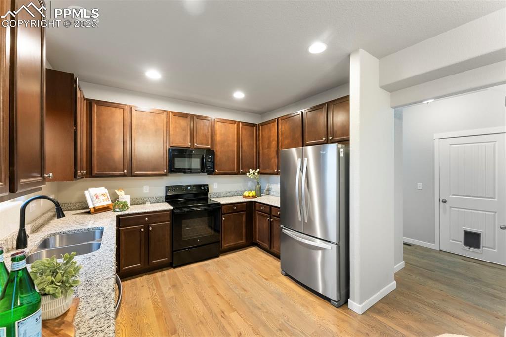 Image 10 of 50: Kitchen featuring black appliances, light stone counters, light wood-style 