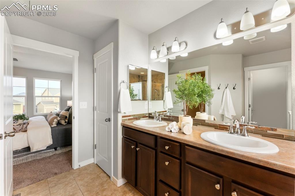 Image 21 of 50: Ensuite bathroom featuring a stall shower, double vanity, and light tile pa