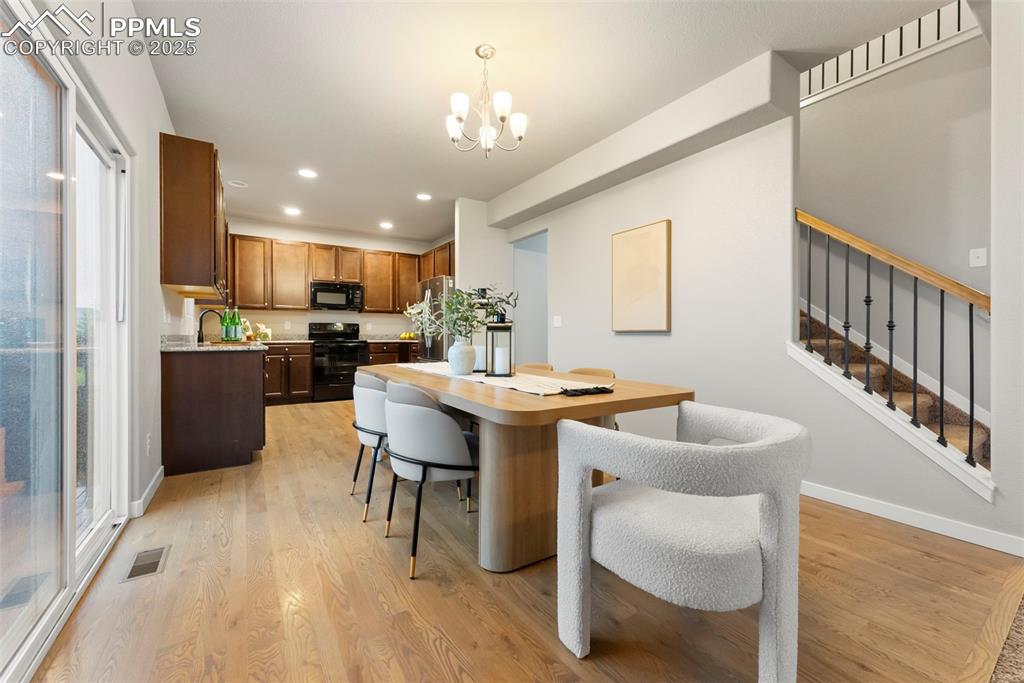 Image 8 of 50: Dining room featuring light wood finished floors, a chandelier, stairs, and