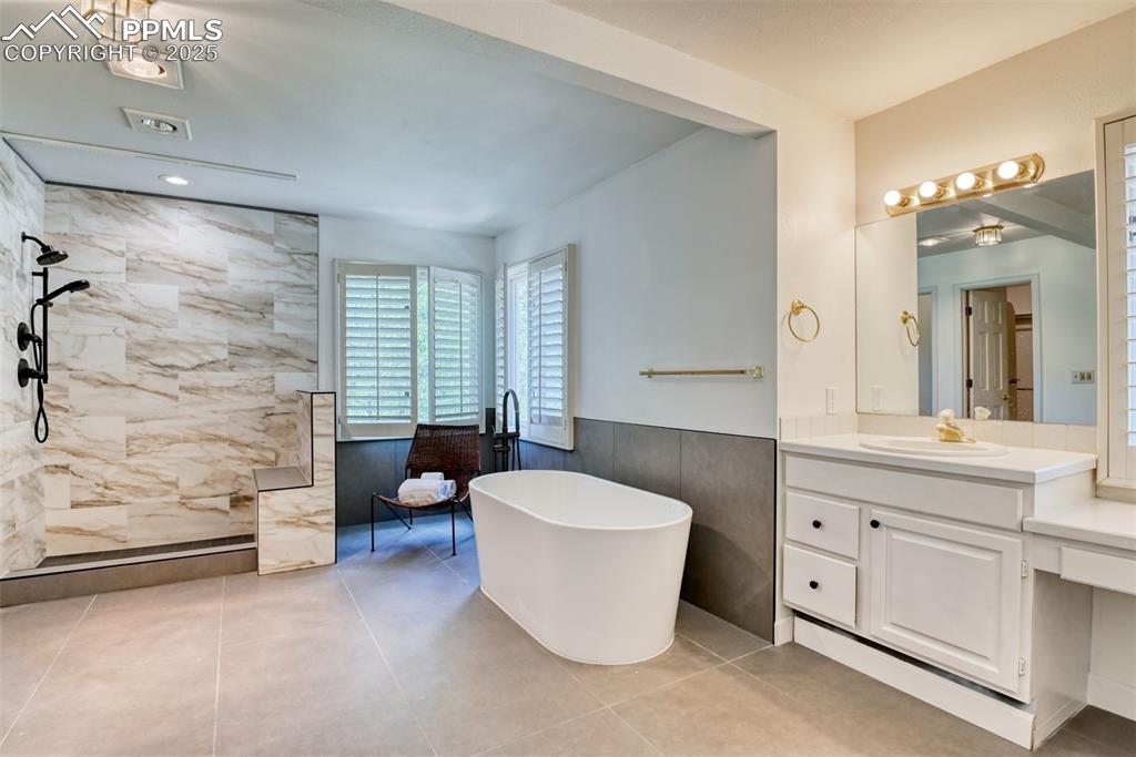 Image 24 of 50: Bathroom featuring walk in shower, a soaking tub, vanity, tile walls, and a