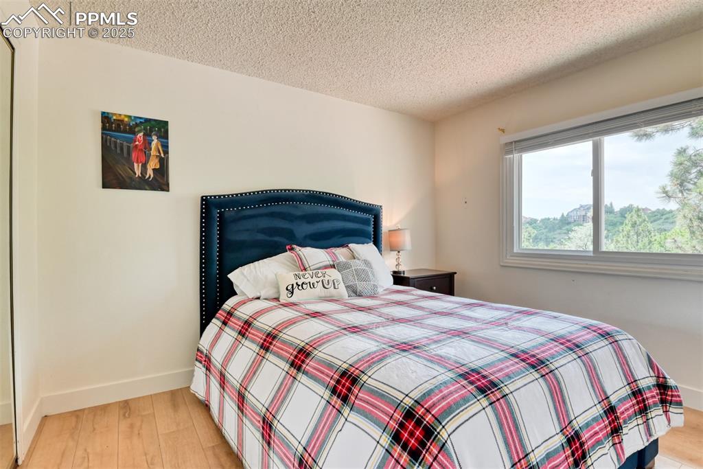 Image 27 of 50: Bedroom with light wood-style floors, a textured ceiling, and baseboards