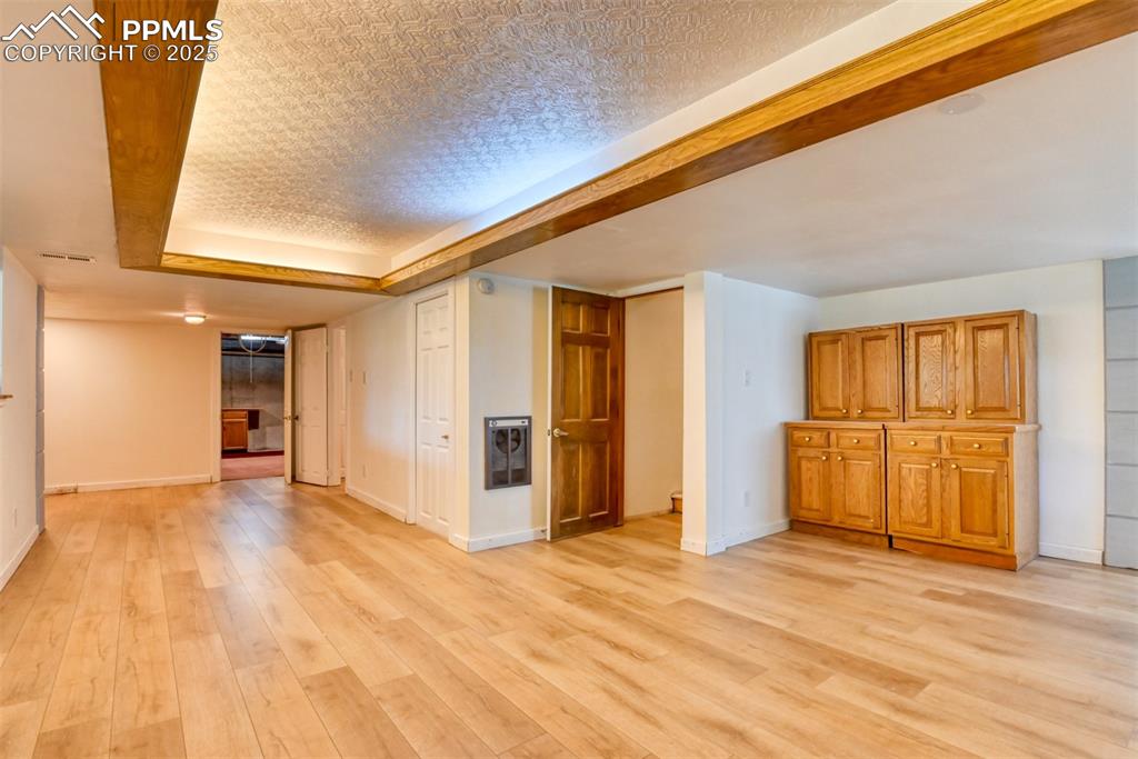 Image 36 of 50: Basement living room with light wood-style flooring, heating unit, baseboar