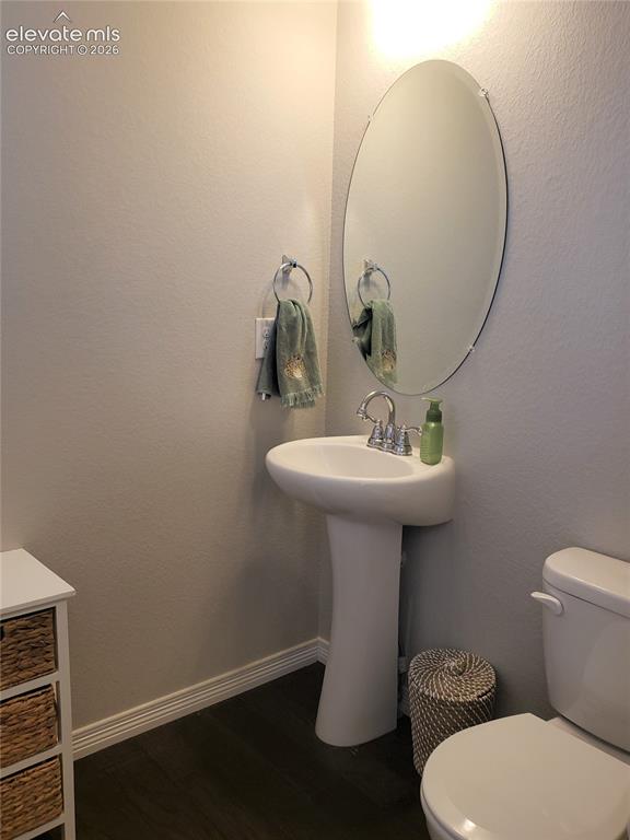 Image 25 of 34: Pedestal sink with chrome faucet, an oval mirror, and dark wood-finish floo
