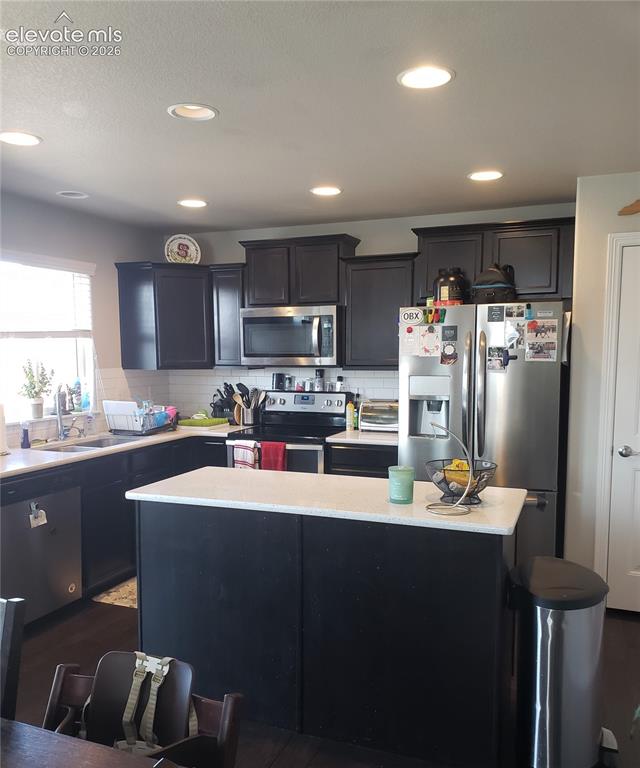 Image 27 of 34: Kitchen featuring dark cabinetry, stainless steel appliances, white counter