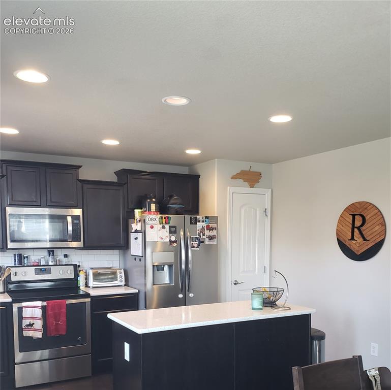 Image 28 of 34: Kitchen featuring dark cabinetry, stainless steel appliances, a subway tile