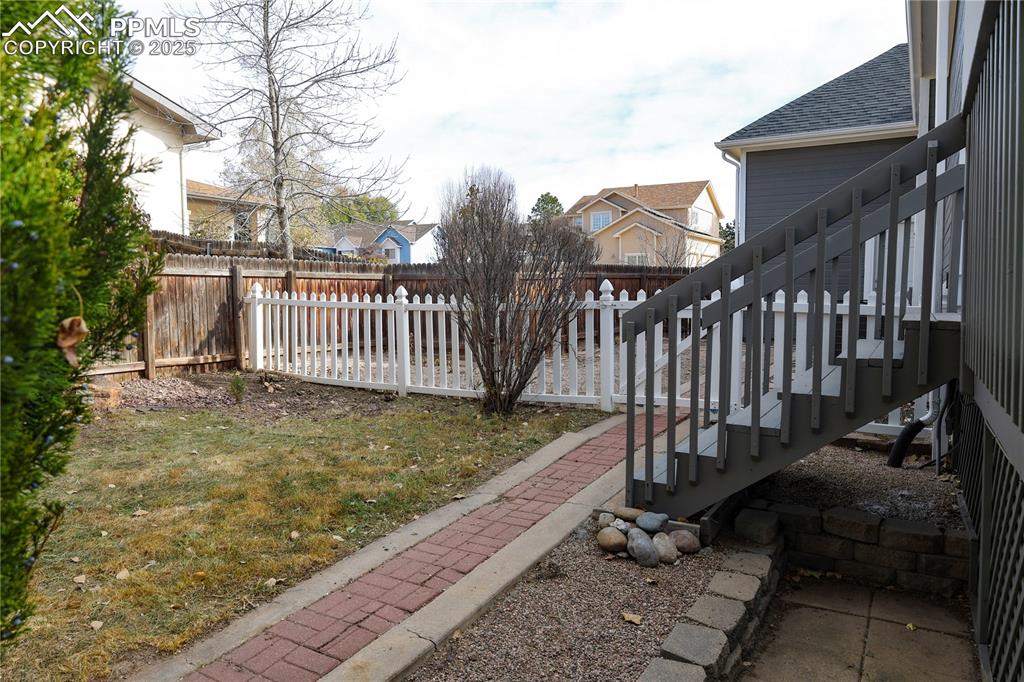 Image 40 of 49: Fenced side yard featuring second stairway to deck.