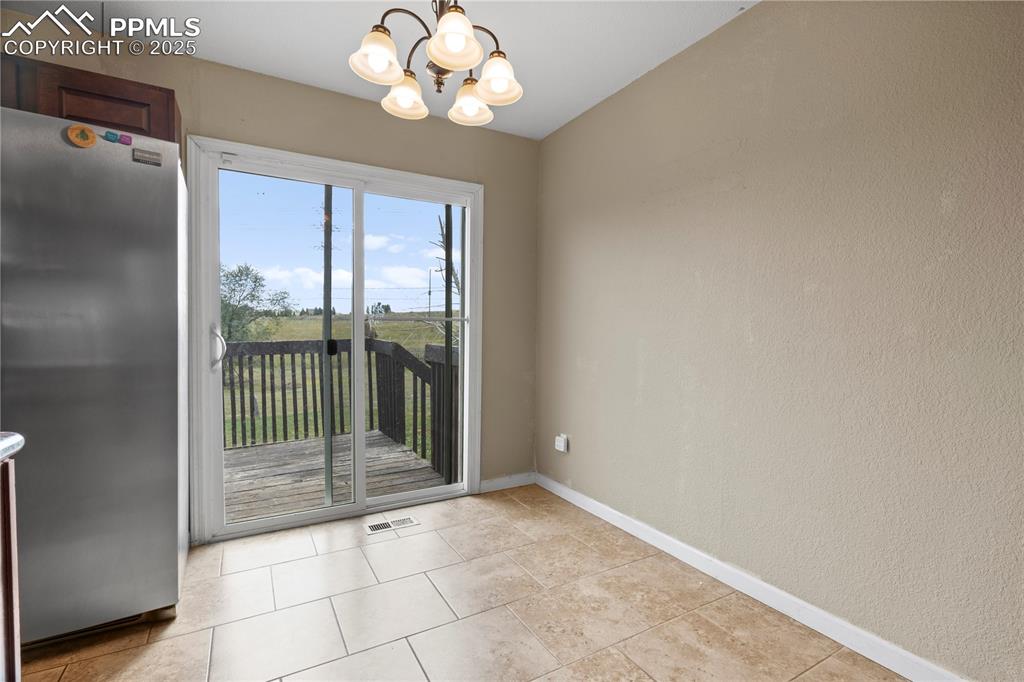 Image 7 of 34: Unfurnished dining area with a chandelier, a textured wall, and light tile 