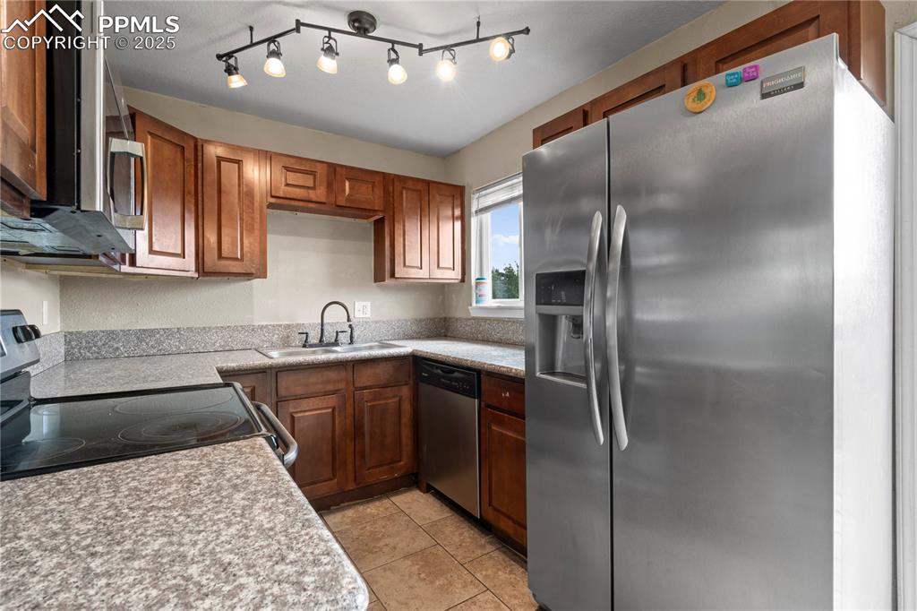 Image 8 of 34: Kitchen with appliances with stainless steel finishes, brown cabinetry, lig