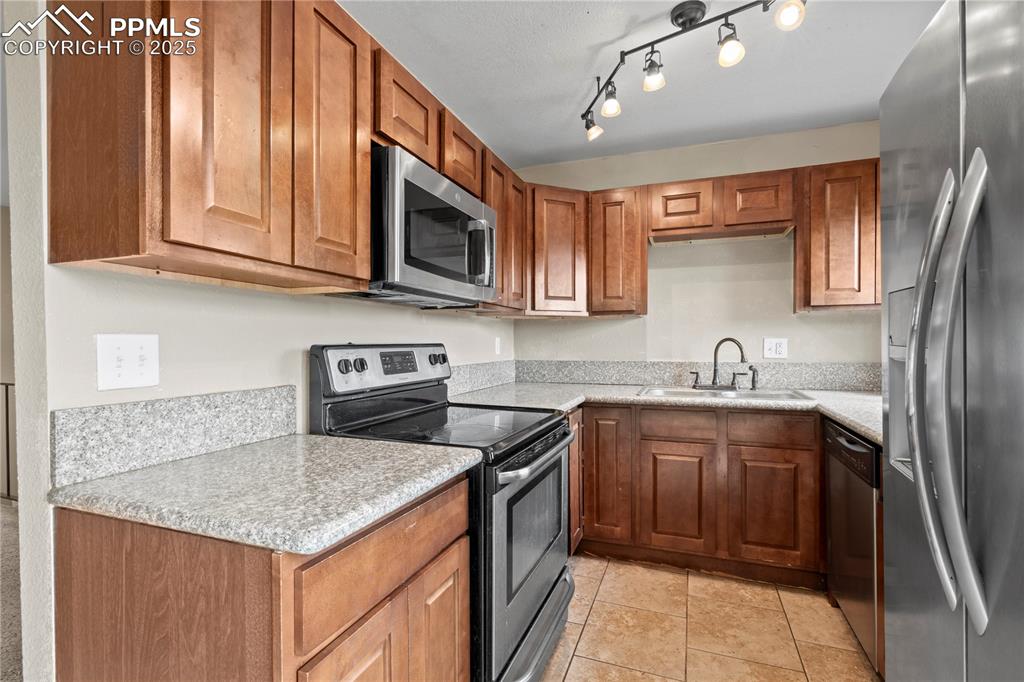 Image 9 of 34: Kitchen with stainless steel appliances, brown cabinets, and light tile pat